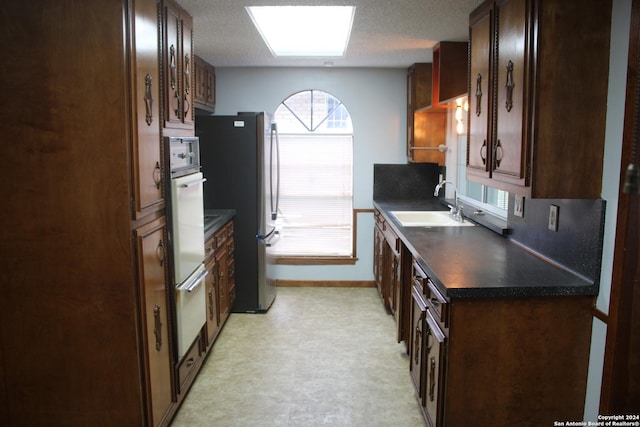 kitchen with sink, a skylight, a textured ceiling, stainless steel refrigerator, and white oven