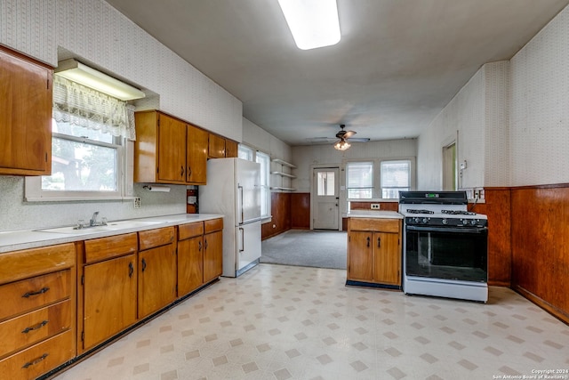 kitchen featuring sink, ceiling fan, fridge, range with gas cooktop, and wood walls