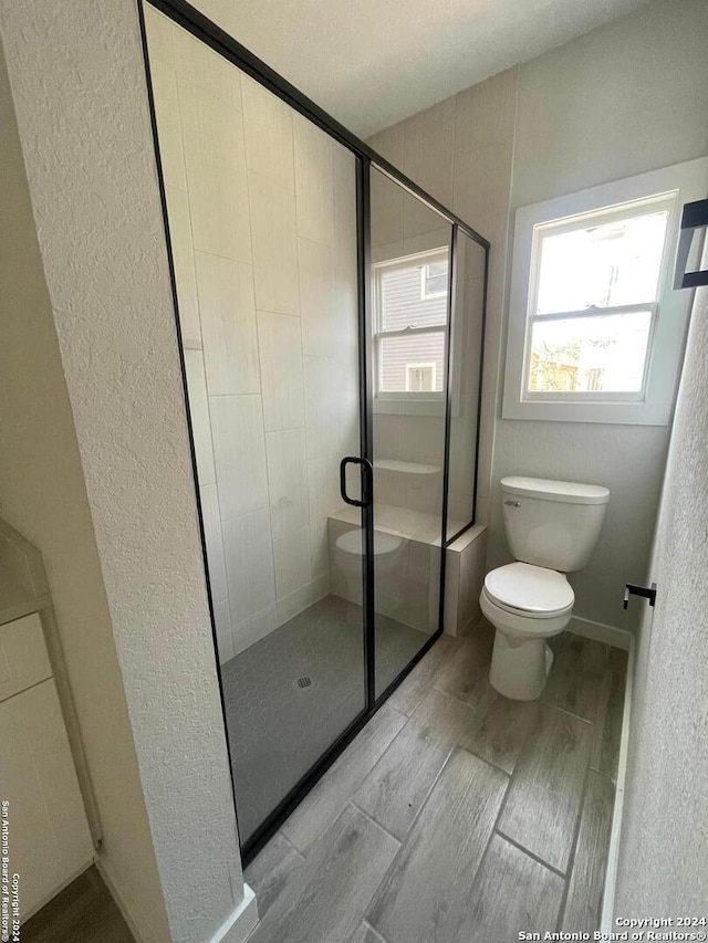 bathroom with hardwood / wood-style floors, walk in shower, and toilet