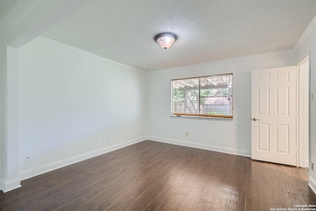 empty room with a textured ceiling, crown molding, and dark wood-type flooring