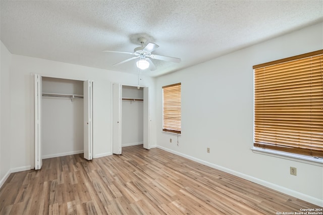 unfurnished bedroom featuring multiple closets, ceiling fan, light hardwood / wood-style flooring, and a textured ceiling