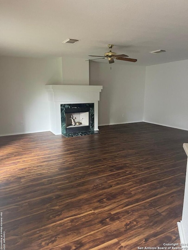 unfurnished living room featuring a premium fireplace, ceiling fan, and dark wood-type flooring