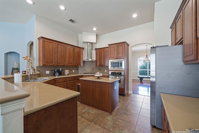 kitchen featuring wall chimney exhaust hood, kitchen peninsula, sink, a center island, and appliances with stainless steel finishes