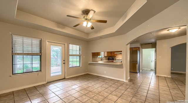 interior space with kitchen peninsula, stainless steel fridge, a raised ceiling, and light tile patterned flooring