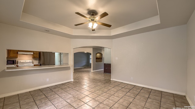 empty room with a tray ceiling, ceiling fan, and light tile patterned floors