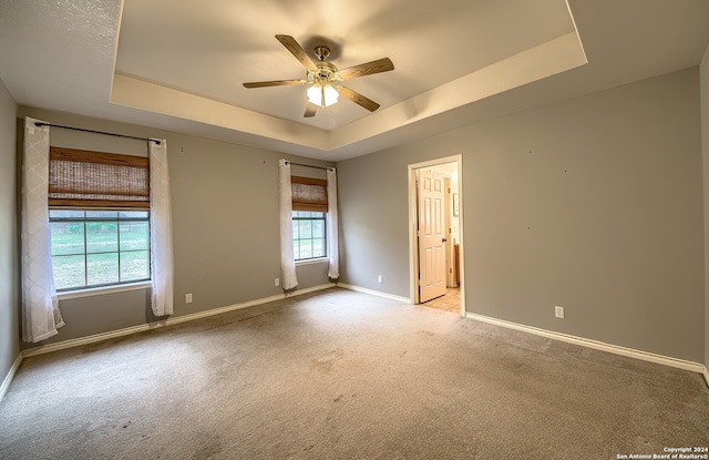 empty room featuring a tray ceiling, ceiling fan, a healthy amount of sunlight, and light colored carpet