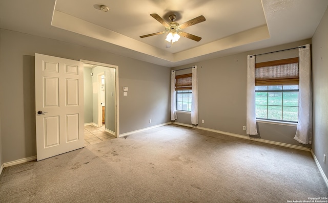 unfurnished bedroom with light colored carpet, a raised ceiling, and ceiling fan