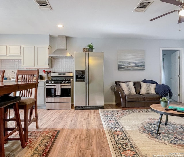 kitchen featuring white cabinetry, wall chimney range hood, backsplash, and appliances with stainless steel finishes