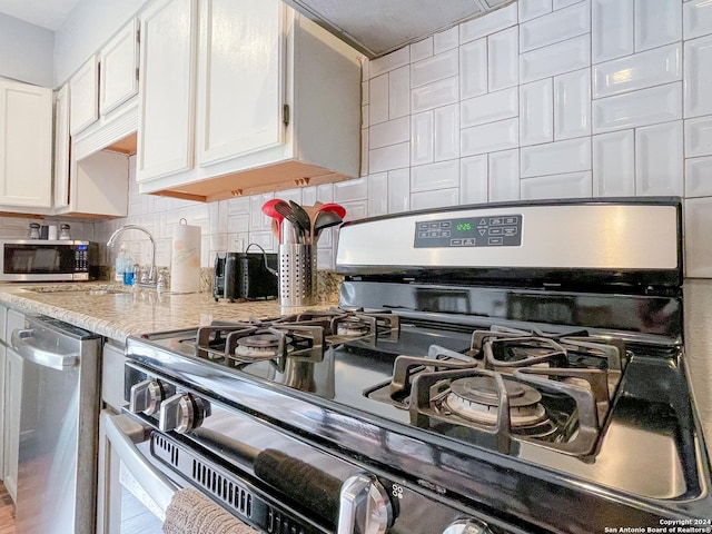 interior details featuring light stone countertops, sink, stainless steel appliances, decorative backsplash, and white cabinets