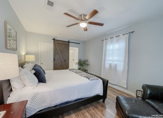 bedroom with a barn door, ceiling fan, and wood-type flooring