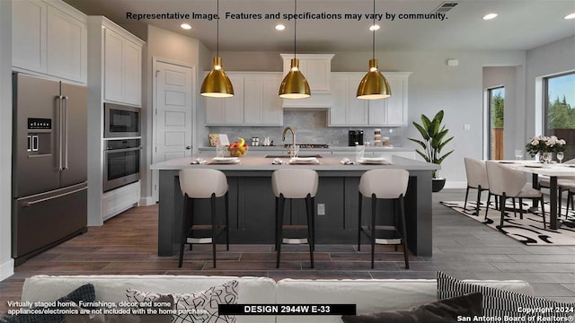 kitchen featuring pendant lighting, stainless steel appliances, white cabinetry, and a center island with sink