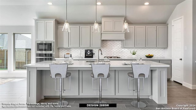 kitchen with sink, a kitchen island with sink, hanging light fixtures, and built in microwave