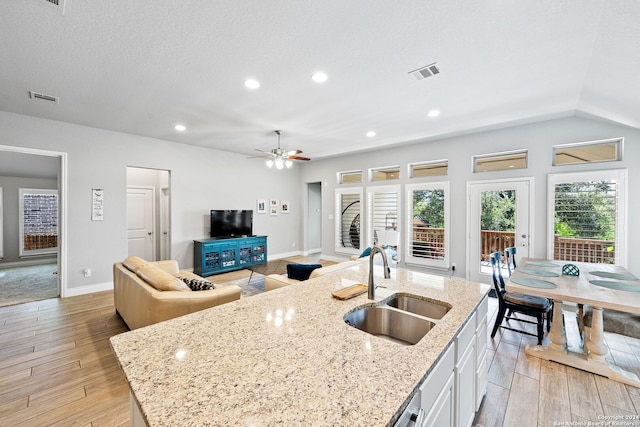 kitchen featuring light stone counters, white cabinetry, sink, and an island with sink