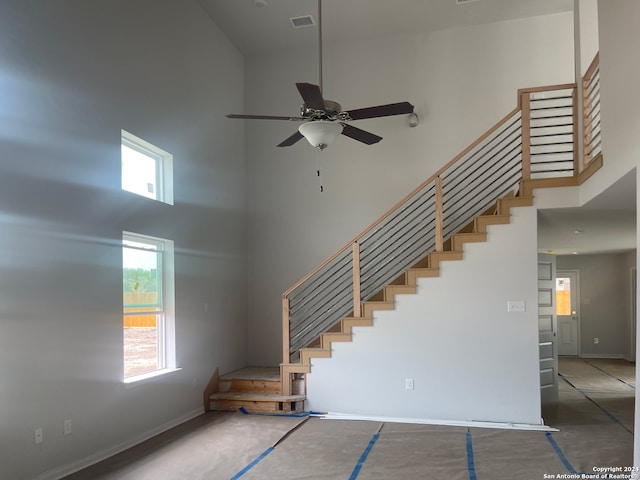 stairs featuring plenty of natural light, ceiling fan, a high ceiling, and concrete floors