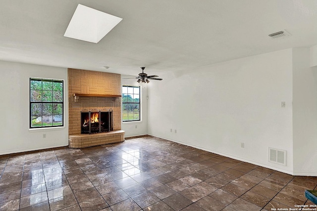 unfurnished living room featuring a skylight, ceiling fan, a fireplace, and dark tile patterned flooring