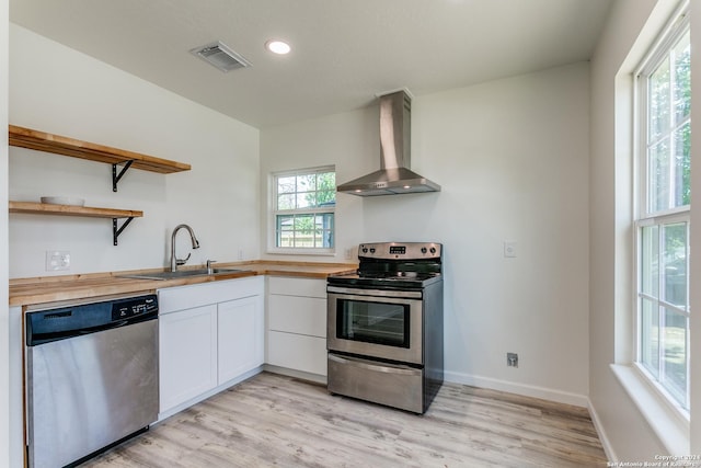 kitchen with white cabinets, sink, wall chimney exhaust hood, butcher block counters, and stainless steel appliances