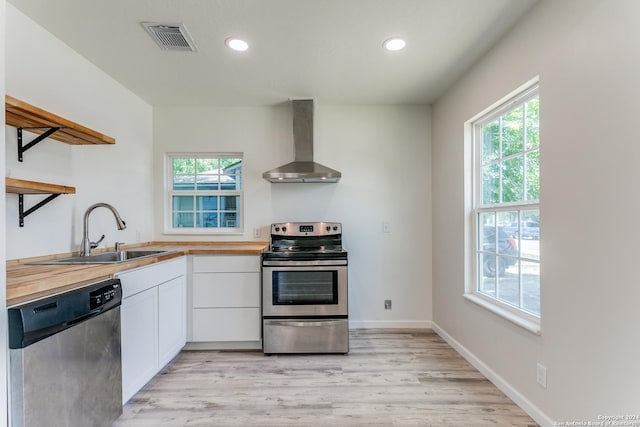 kitchen featuring sink, wall chimney range hood, wooden counters, white cabinets, and appliances with stainless steel finishes