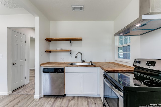 kitchen featuring sink, wall chimney exhaust hood, butcher block countertops, white cabinets, and appliances with stainless steel finishes