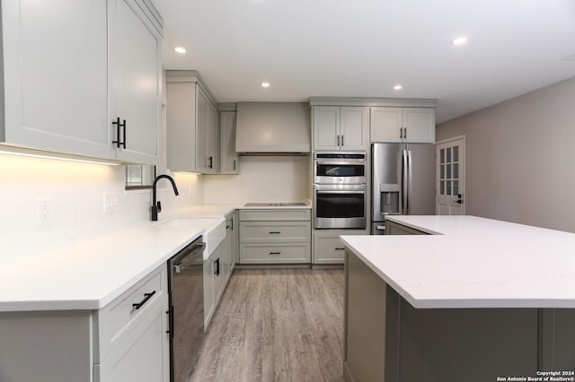 kitchen with sink, stainless steel appliances, light hardwood / wood-style flooring, gray cabinets, and custom range hood