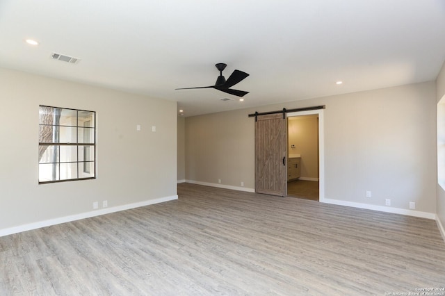 spare room featuring a barn door, ceiling fan, and light hardwood / wood-style flooring