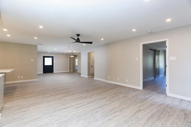 unfurnished living room featuring ceiling fan, a barn door, and light hardwood / wood-style flooring