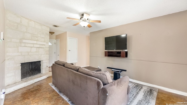 living room with a textured ceiling, ceiling fan, and a stone fireplace