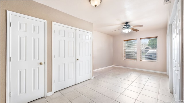 unfurnished bedroom with multiple closets, ceiling fan, and light tile patterned floors