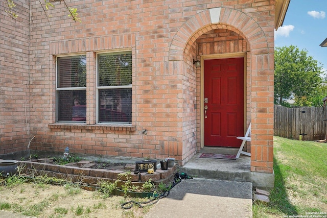 doorway to property featuring brick siding and fence