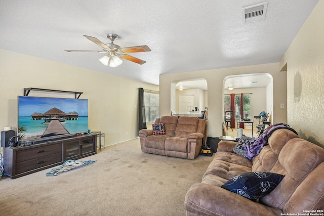 carpeted living room with arched walkways, visible vents, a textured ceiling, and ceiling fan