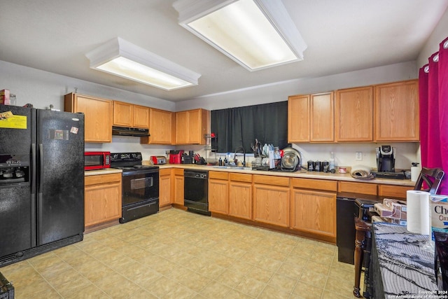 kitchen with black appliances, light countertops, under cabinet range hood, and a sink