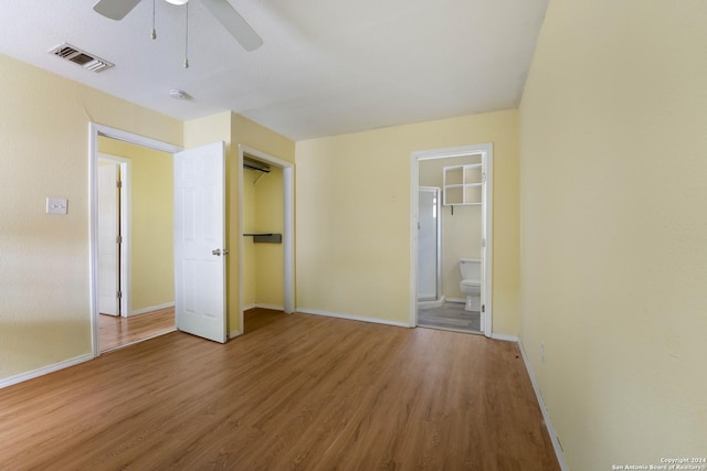 unfurnished bedroom featuring wood-type flooring, a closet, ensuite bath, and ceiling fan