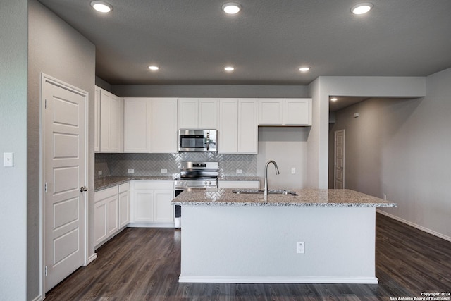 kitchen with sink, appliances with stainless steel finishes, light stone countertops, white cabinets, and a center island with sink