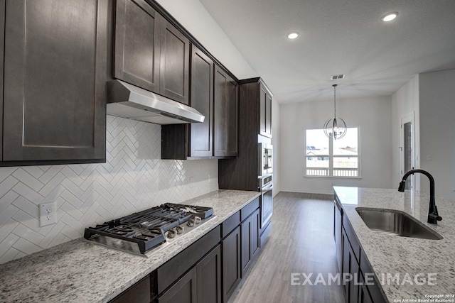 kitchen featuring light stone countertops, stainless steel appliances, decorative backsplash, sink, and a notable chandelier