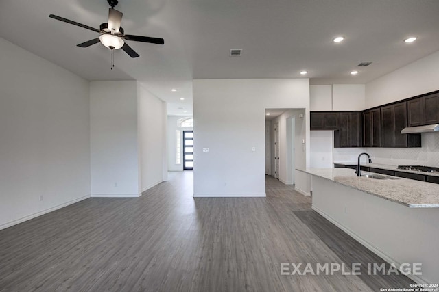 kitchen with backsplash, wood-type flooring, sink, dark brown cabinetry, and light stone countertops