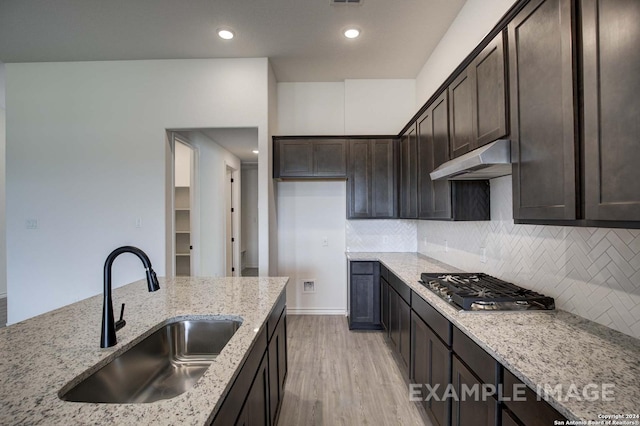 kitchen with stainless steel gas stovetop, dark brown cabinets, light stone counters, and sink