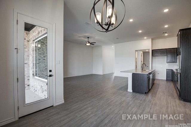 kitchen featuring ceiling fan with notable chandelier, pendant lighting, dark hardwood / wood-style flooring, tasteful backsplash, and a center island with sink