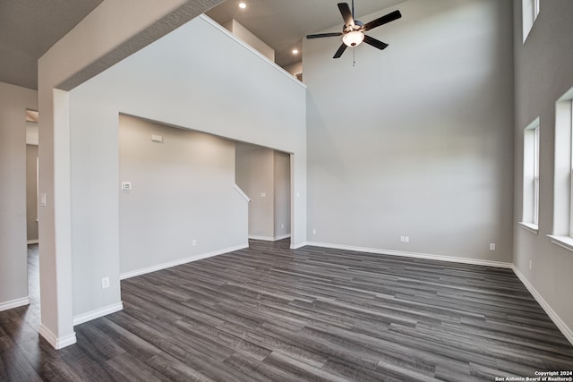 unfurnished living room featuring ceiling fan, a towering ceiling, and dark hardwood / wood-style floors