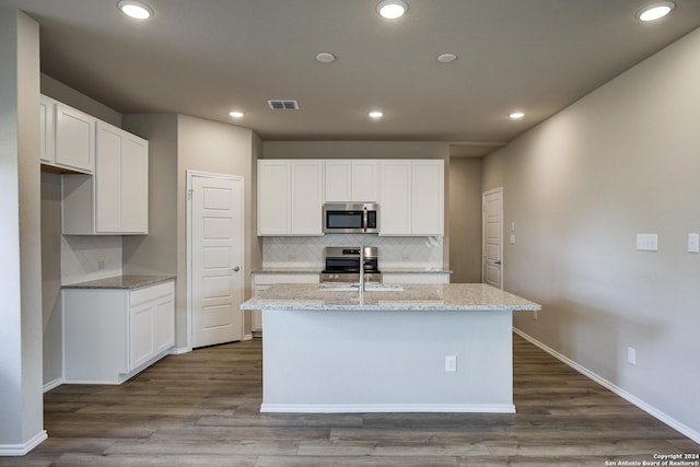 kitchen featuring stainless steel appliances, visible vents, decorative backsplash, and a center island with sink