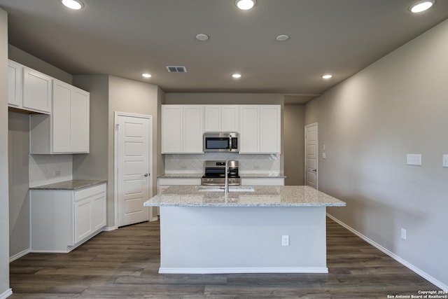 kitchen featuring an island with sink, light stone countertops, backsplash, and appliances with stainless steel finishes