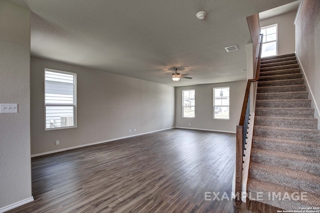 unfurnished living room with a wealth of natural light, ceiling fan, and dark wood-type flooring