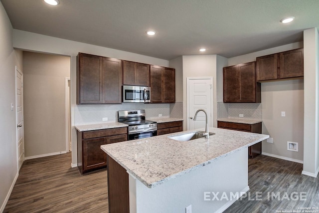 kitchen featuring a center island with sink, sink, decorative backsplash, light stone countertops, and stainless steel appliances