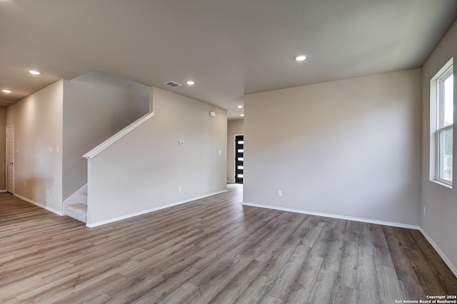 unfurnished living room with plenty of natural light, visible vents, recessed lighting, wood finished floors, and stairway