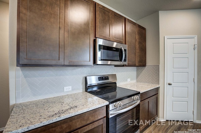 kitchen featuring dark hardwood / wood-style flooring, backsplash, stainless steel appliances, and light stone counters