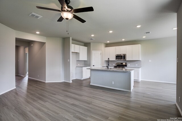 kitchen featuring light stone counters, a center island with sink, white cabinets, and appliances with stainless steel finishes