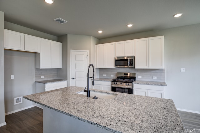 kitchen with appliances with stainless steel finishes, sink, white cabinets, light stone countertops, and a center island with sink