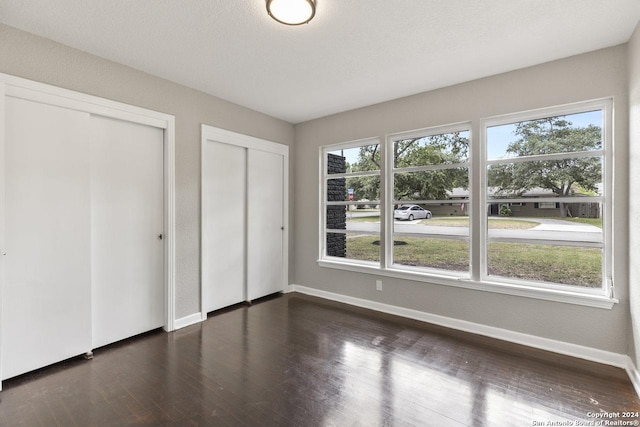 unfurnished bedroom featuring dark wood-type flooring, multiple windows, and multiple closets