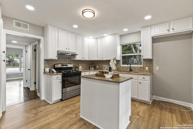 kitchen featuring white cabinets, light wood-type flooring, a center island, and stainless steel gas range oven