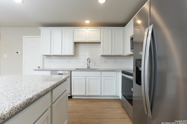 kitchen featuring backsplash, white cabinets, sink, light stone countertops, and stainless steel appliances