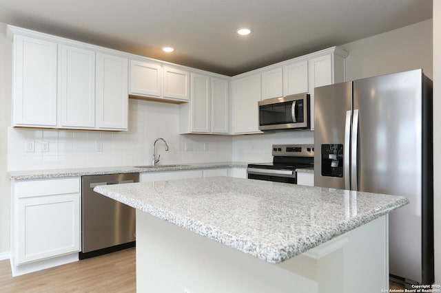 kitchen with a center island, stainless steel appliances, light stone counters, light hardwood / wood-style flooring, and white cabinets