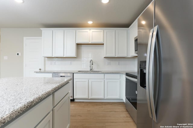 kitchen featuring backsplash, white cabinets, sink, appliances with stainless steel finishes, and light stone counters